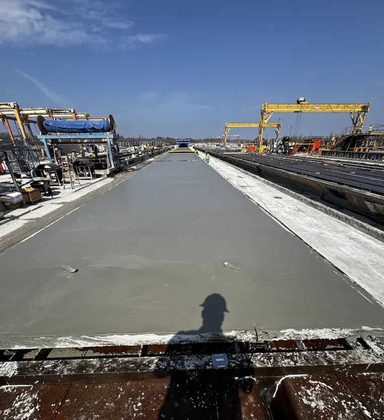 Freshly cast prestressed member running the length of a casting bed at NAPCO Precast, with gantry cranes over the yard