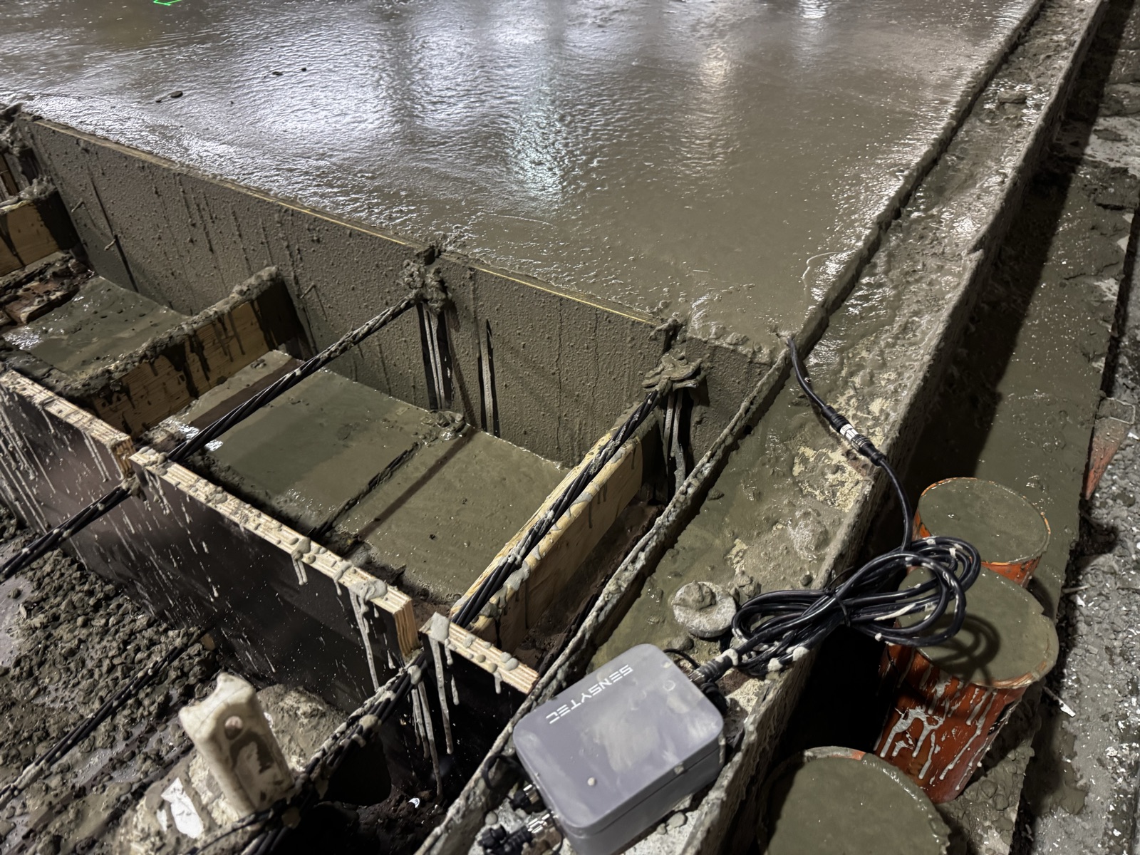 SensyCast wireless concrete sensor mounted on precast formwork next to a fresh concrete pour
